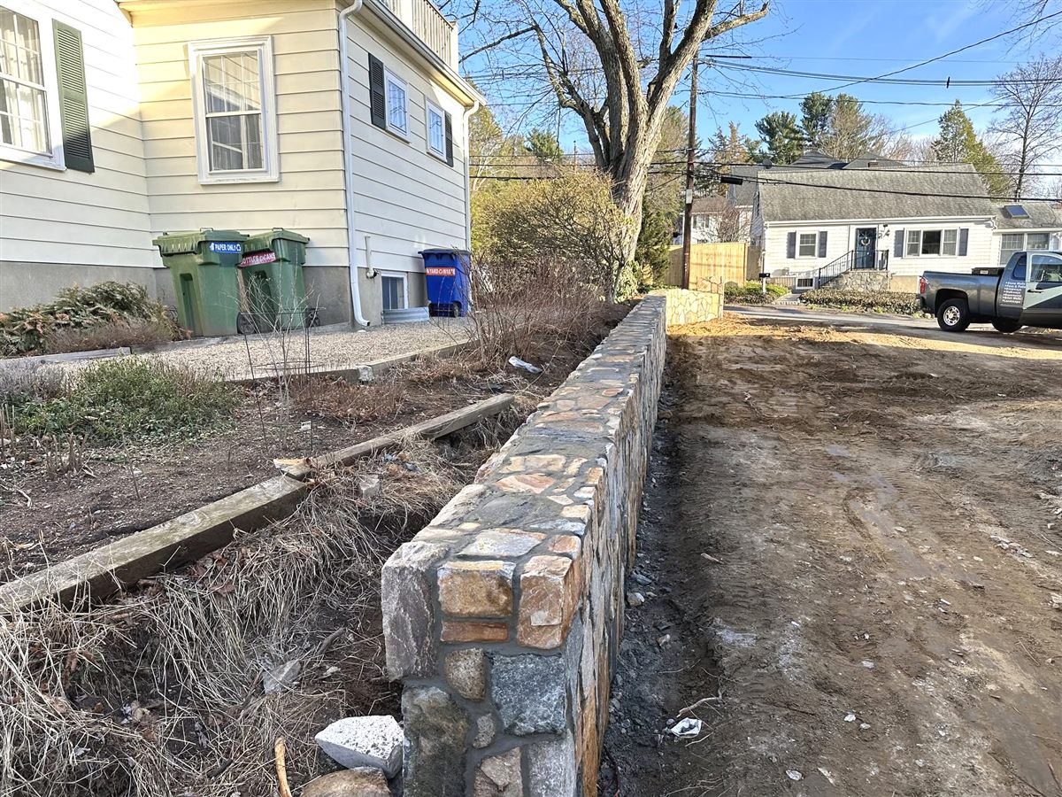 Completed stone wall running along a driveway with the North Colony Masonry truck parked at the curb