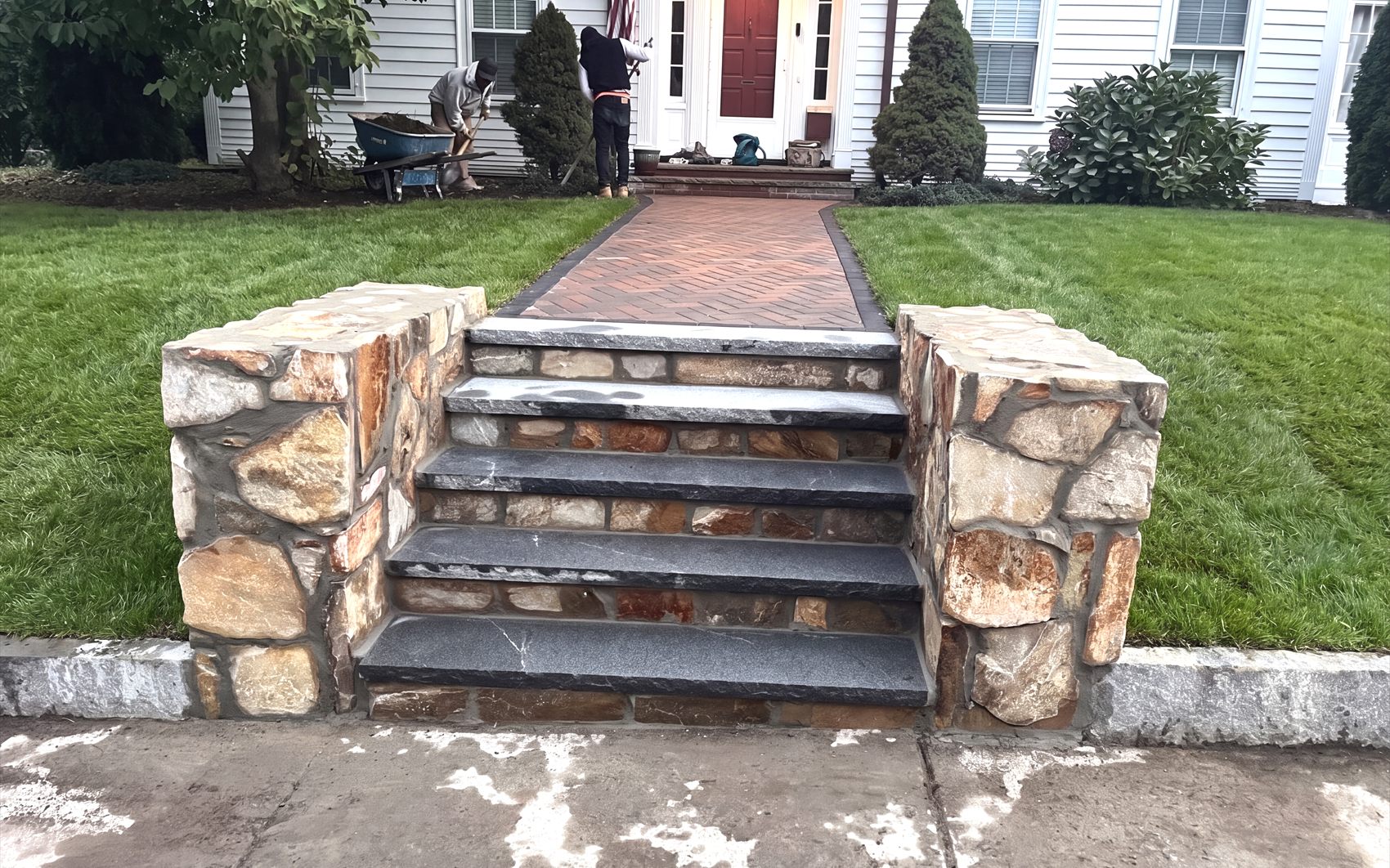 Stone faced entry steps with cut treads leading to a brick walkway and the front door of a Massachusetts home