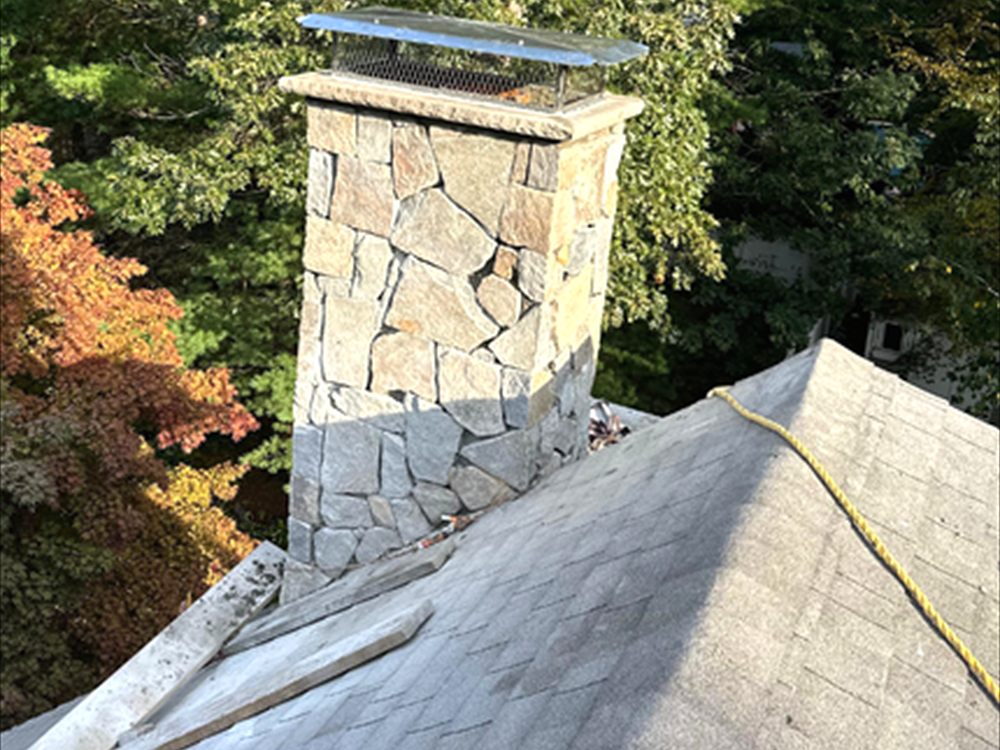 Stone faced chimney with a cap rising through a shingled roof