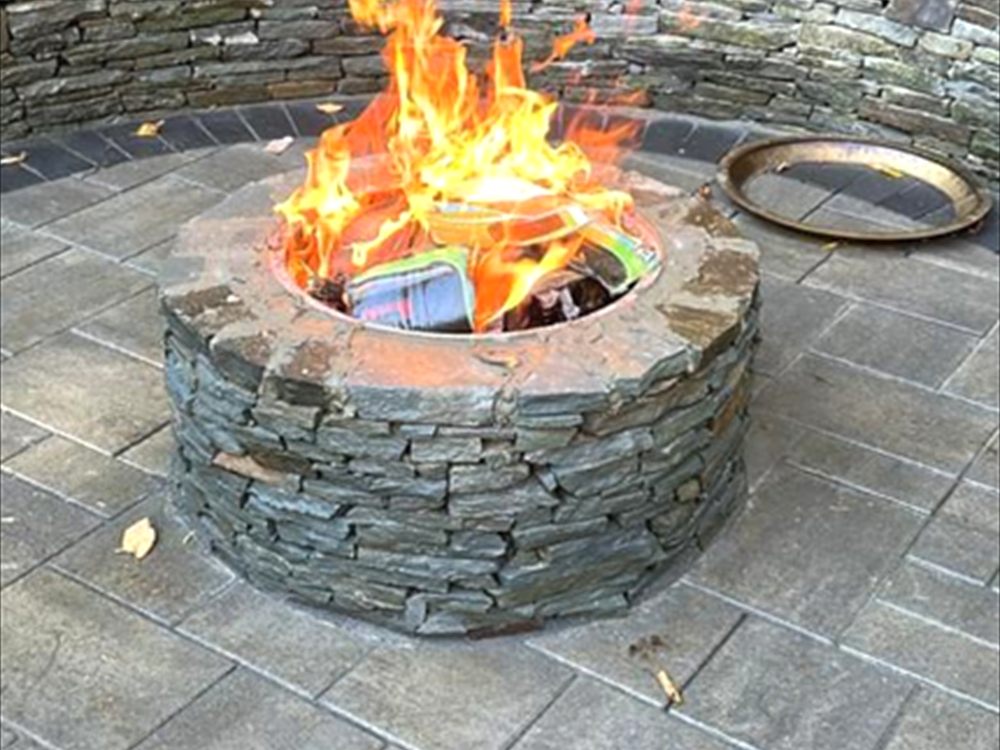 Round stone fire pit with a live fire set into a paver patio with a curved seat wall