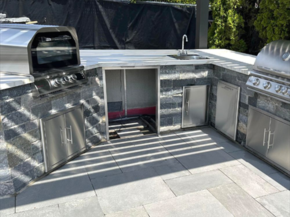 Outdoor kitchen with stainless grill, sink and stone counter on a stone terrace