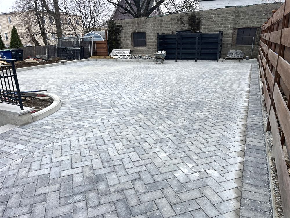Large herringbone paver courtyard enclosed by a fence and a block wall