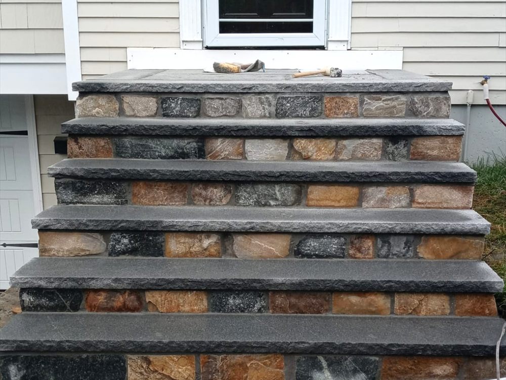 Stone faced entry steps with cut treads beside a house