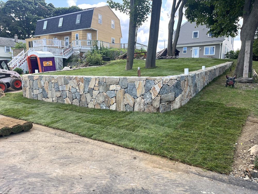 Long stone retaining wall with fresh sod laid along a residential front yard